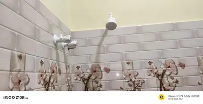 a bathroom with a white tile wall with flowers on it at S M LODGe in Dharmapuri