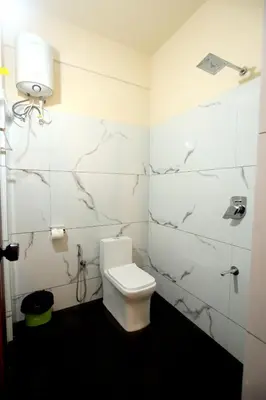 a bathroom with a toilet and a white tiled wall at Skylark Home in Mananthavady