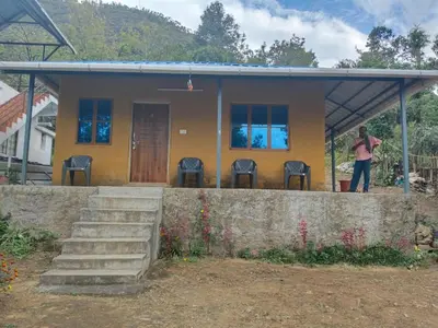 a woman standing in front of a house at BREEZE GARDEN MUD HOUSE Home Stay in Kanthalloor