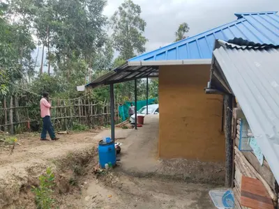 a man standing next to a building with a blue roof at BREEZE GARDEN MUD HOUSE Home Stay in Kanthalloor