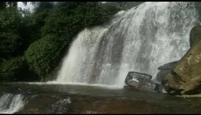 a waterfall in front of a pool of water at Munnar Wood valley in Munnar