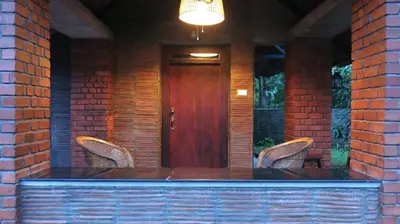 a porch with two chairs and a wooden door at Clayfingers Art Cottage in Trichūr