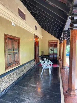 a porch with two white chairs and a table at Aravanazhi tharavadu in Thirunelli