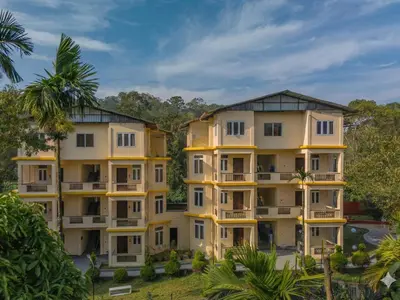 a large yellow building with trees in the background at The Hosteller Bam Coorg in Madikeri