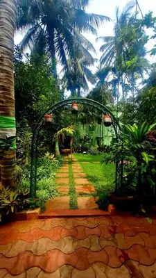 a garden with an arch and a walkway with palm trees at NesaraVana - Ecostay in Hārohalli