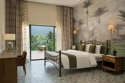 a bedroom with a bed and a desk and a window at The Ranch Kakkadampoyil - a VKation Experience in Kakkadampoyil