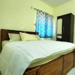 a bedroom with a large white bed with blue curtains at Sai Home Stay in Marudhamalai