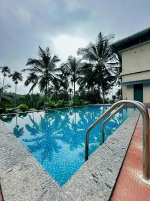 a swimming pool with palm trees in the background at Gcc Saffron in Wayanad
