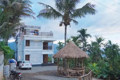 a white house with a palm tree and a building at Wildlife Homestay in Kanthalloor