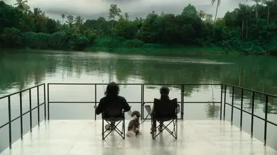 two people and a dog sitting in chairs by a lake at Vanantara - Riverside Eco Retreat in Ernakulam