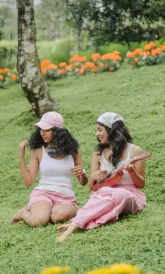 two young women sitting on the grass in a park at Woodshade resort in Wayanad