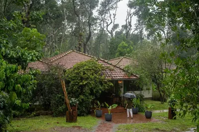 a woman holding an umbrella in front of a house at Chetty's Mane by Raho - Estate-View Heritage Stay in Siddapur