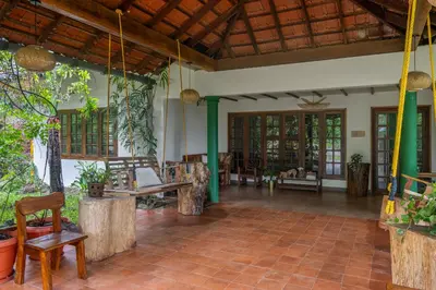 a living room with chairs and tables and windows at Chetty's Mane by Raho - Estate-View Heritage Stay in Siddapur