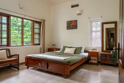 a bedroom with a bed and a mirror and windows at Chetty's Mane by Raho - Estate-View Heritage Stay in Siddapur