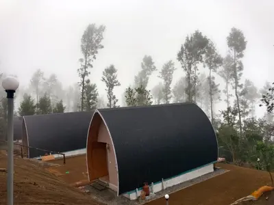 a large building with a black roof in front of a forest at Bhramaram resort in Kanthalloor