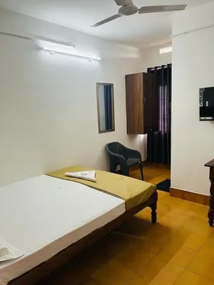 a bedroom with a bed and a chair in it at Vinayaka Tourist Home in Kozhikode