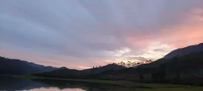 a sunset over the mountains with a river in the foreground at Brindavan Lake Resort in Munnar