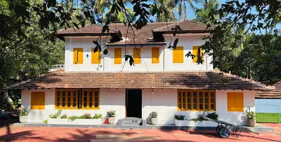a white house with yellow shuttered windows at Idanazhi the corridor in Kozhikode