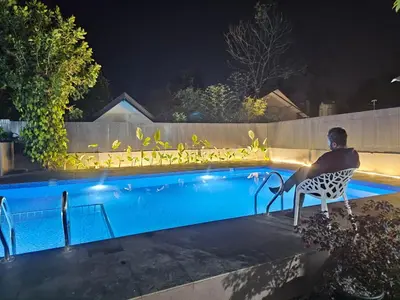 a man sitting in a chair next to a swimming pool at night at Mount Wave Holiday Pool Villa in Wayanad