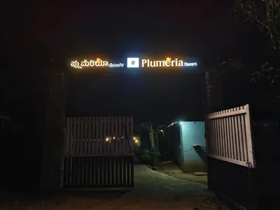 a gate to a driveway at night with a sign at Plumeria Resort Coorg in Kushālnagar
