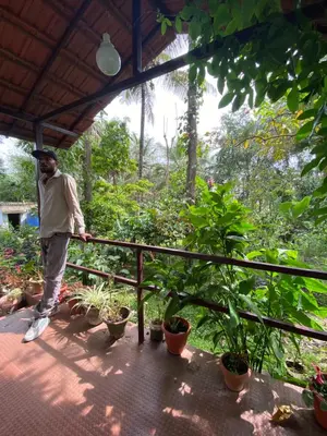 a man standing on a porch with plants at Coorg jungle Cottage in Kushālnagar