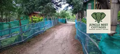 a dirt road with a sign on a fence at Jungle Mist Cottages in Masinagudi