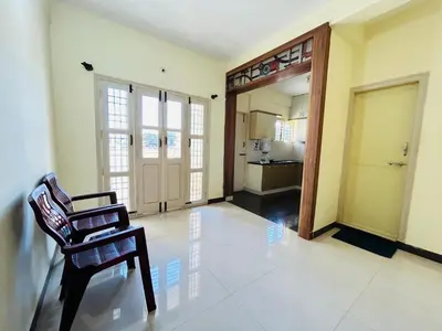 a living room with a chair and a kitchen at Raya 2 bhk flats in Mysore
