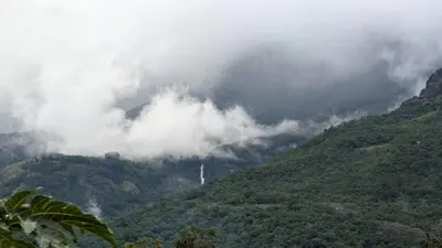 a view of a mountain with clouds on it at Magizh Kudil The Mud House in Marayoor
