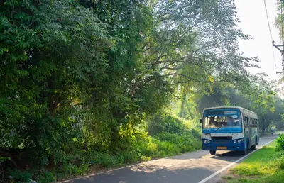 a blue bus driving down a road with trees at Pollachi Riverhouse, A CGH Earth Saha experience in Pollāchi