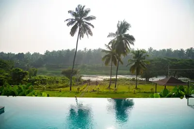 a view of a pool with palm trees in the background at Pollachi Riverhouse, A CGH Earth Saha experience in Pollāchi