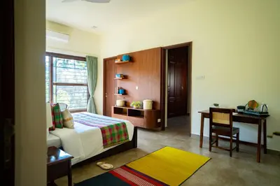 a bedroom with a bed and a desk and a table at Pollachi Riverhouse, A CGH Earth Saha experience in Pollāchi
