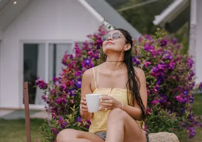 a woman sitting on a chair holding a cup of coffee at Gardenia Pool Resort Kanthalloor by VOYE HOMES Mountain View Stay Near Bhramaram view Point in Kanthalloor