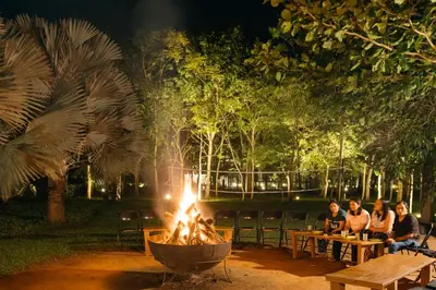 a group of people sitting around a fire pit at night at Discovery Village Kabini in Antarasante
