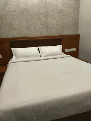a white bed with a wooden headboard and white sheets at Hotel Riviera in Mananthavady