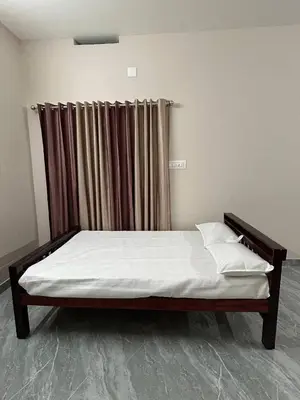 a bed sitting in a room with a curtain at Cosy Stays, 2 Adjacent Apartments in Irinjalakuda in Irinjālakuda