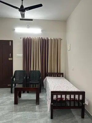 a bedroom with a bed and two chairs and a ceiling fan at Cosy Stays, 2 Adjacent Apartments in Irinjalakuda in Irinjālakuda