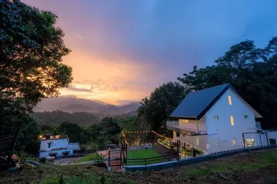 a house on a hill with a sunset in the background at SUKOON Stays - Nestled among the misty hills and lush forests in Vythiri