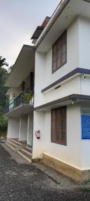 a white house with red windows and a balcony at Green palace service villa in Kalpetta