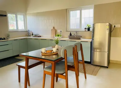 a kitchen with a table and a stainless steel refrigerator at Nesara Home Stay Mysuru in Mysore