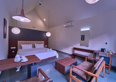 a bedroom with a bed and a table and chairs at Achutham Cottages Wayanad by VOYE HOMES in Padinjarathara