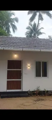 a white house with a door and a palm tree at Katadi beach coral cottage in Thanniyam