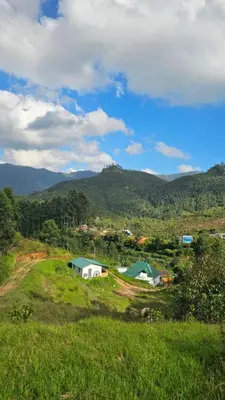 a green field with houses and mountains in the background at Bluehood WildScape in Vattavada