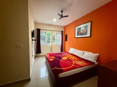 a bedroom with an orange wall with a bed and a window at NILGIRIS Inn in Kotagiri