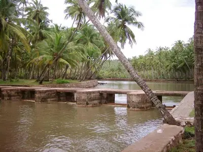 a body of water with palm trees and a bridge at legacy beach stay kannur in Kannur