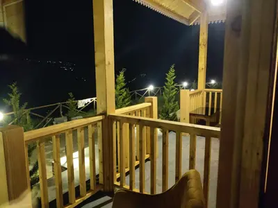 a balcony with a table and a chair at night at Cloudy Nandy Hills Poombarai in Kūkkāl