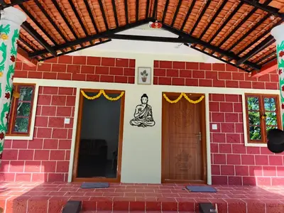 a red brick house with a wooden roof and two doors at JK Cottages in Suntikoppa