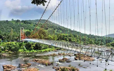 a suspension bridge over a river with a river at Jackroot Heritage wood villa Athirappilly in Kallana
