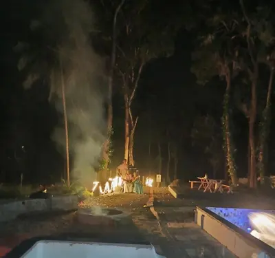 a group of people sitting around a fire at night at The Cool Cottage at gaya3farms in Palakkad