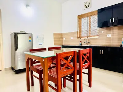 a kitchen with a table and four chairs and a refrigerator at Anandha Vibes in Guruvāyūr
