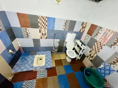 a bathroom with a toilet and a mosaic tile wall at rivers edge homestay in Viripara